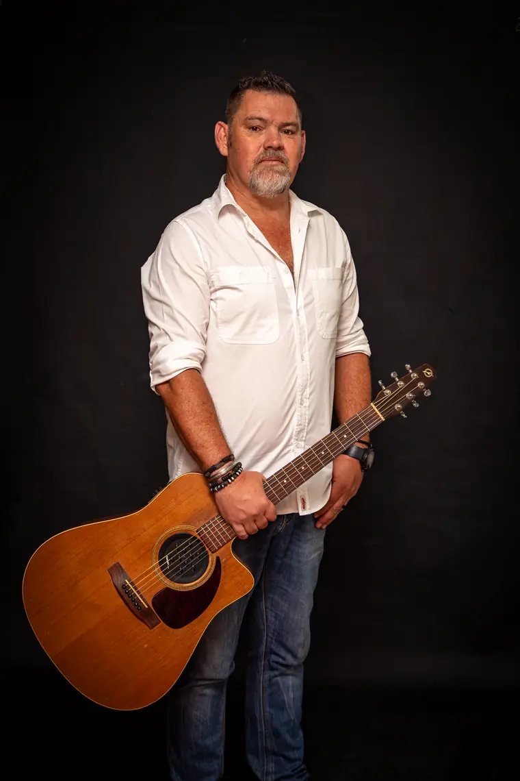 Wynand Strydom staan met sy kitaar teen ’n donker agtergrond