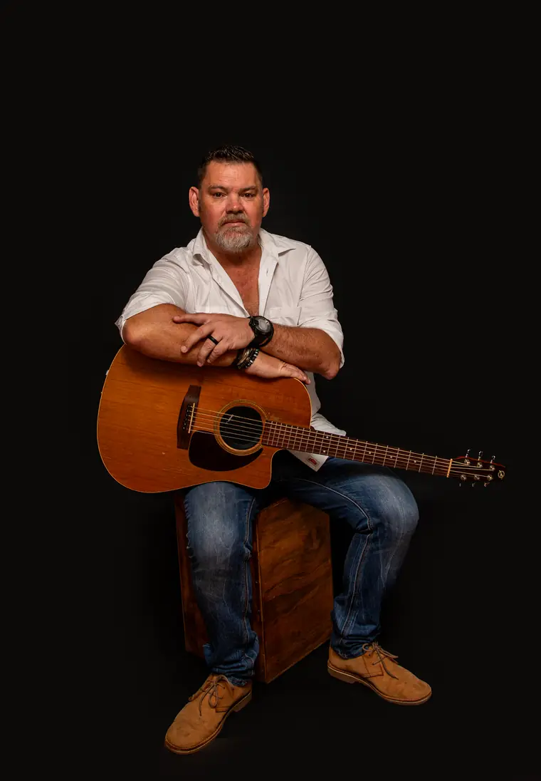 Wynand Strydom op ’n kruk, kitaar in die hand